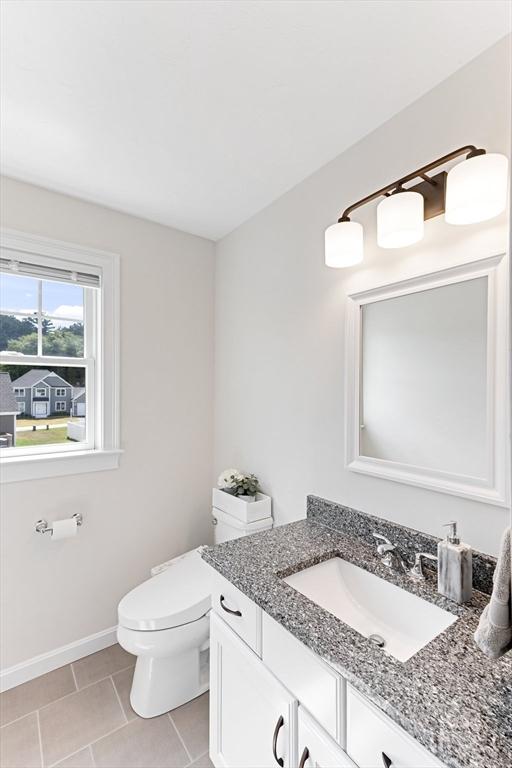 half bathroom with toilet, tile patterned floors, baseboards, and vanity