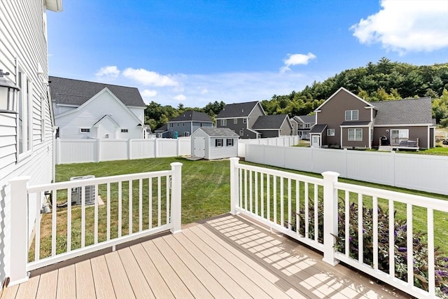 wooden terrace featuring a storage shed, a lawn, a fenced backyard, a residential view, and an outdoor structure