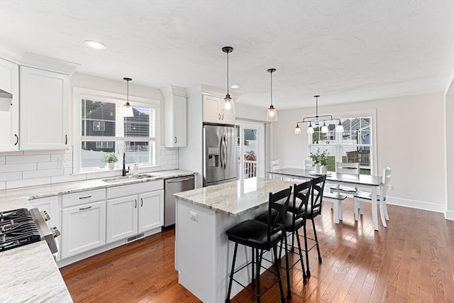 kitchen with stainless steel appliances, a kitchen island, a sink, white cabinets, and pendant lighting