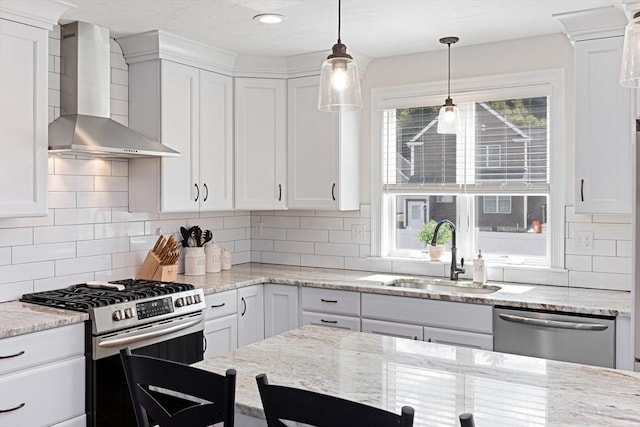 kitchen featuring pendant lighting, stainless steel appliances, white cabinets, a sink, and wall chimney range hood