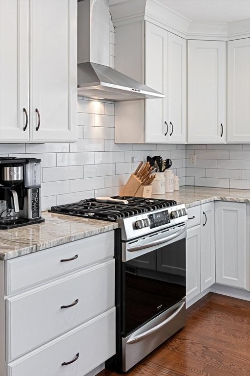 kitchen with white cabinets, stainless steel gas range, light stone countertops, dark wood-style floors, and wall chimney exhaust hood