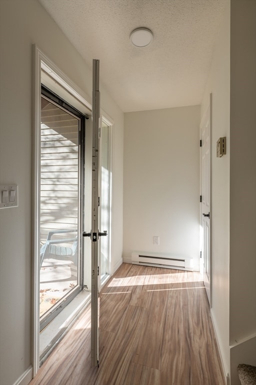 hall with a textured ceiling, light hardwood / wood-style floors, and a baseboard radiator