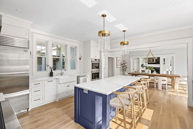 kitchen featuring appliances with stainless steel finishes, sink, light stone counters, light wood-type flooring, and white cabinets