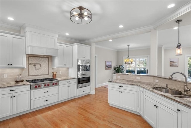 kitchen with appliances with stainless steel finishes, white cabinets, a sink, and decorative light fixtures