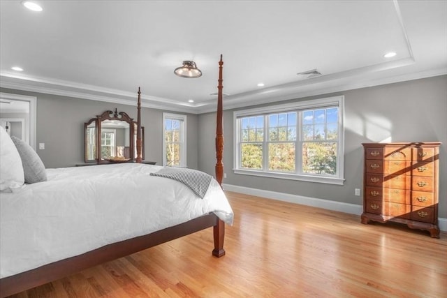 bedroom with ornamental molding, light wood-type flooring, a raised ceiling, and visible vents