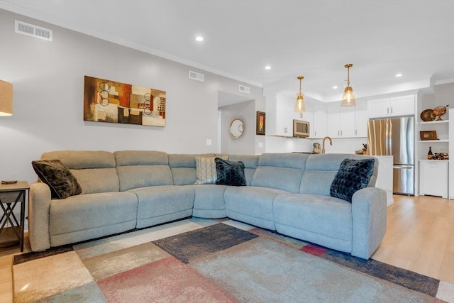 living area with recessed lighting, visible vents, light wood-style floors, and ornamental molding