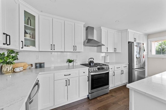 kitchen with white cabinets, wall chimney exhaust hood, light stone counters, and stainless steel appliances