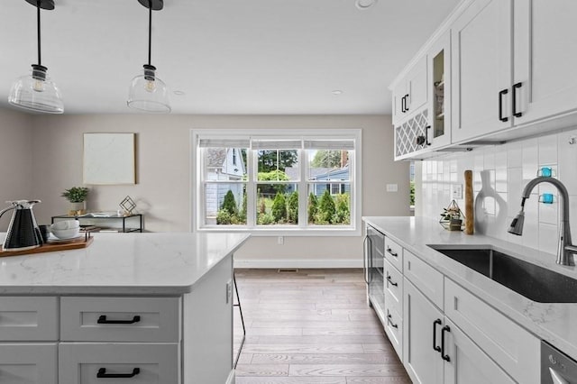 kitchen featuring light stone countertops, sink, pendant lighting, white cabinets, and light wood-type flooring