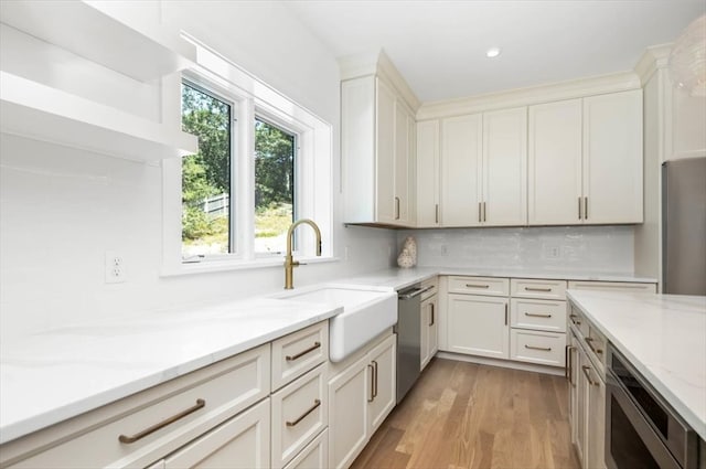 kitchen with appliances with stainless steel finishes, light stone countertops, light wood-type flooring, sink, and backsplash