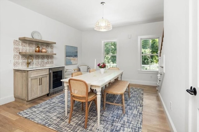 dining room with beverage cooler, light wood-style flooring, and baseboards