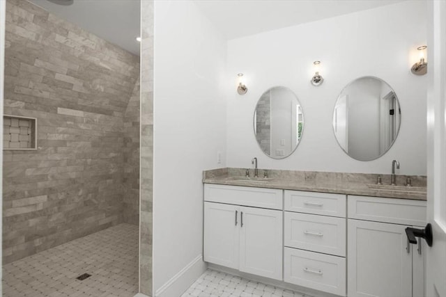 bathroom featuring double vanity, walk in shower, a sink, and baseboards