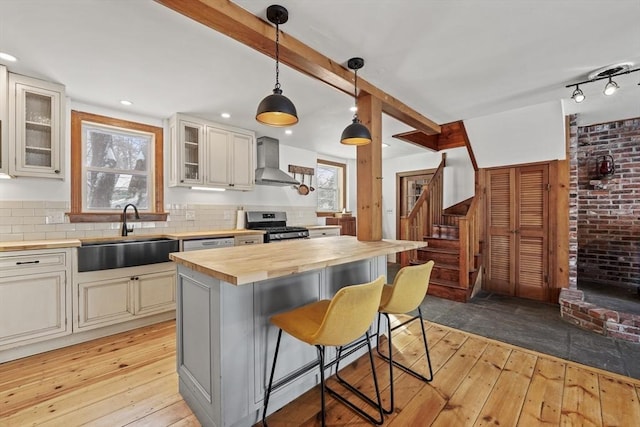 kitchen with wood counters, sink, a center island, gas stove, and wall chimney range hood