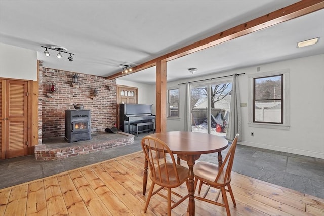 dining space featuring wood-type flooring, a wood stove, and beam ceiling