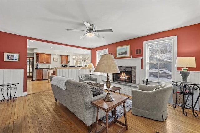 living room featuring ceiling fan, a stone fireplace, and light hardwood / wood-style flooring