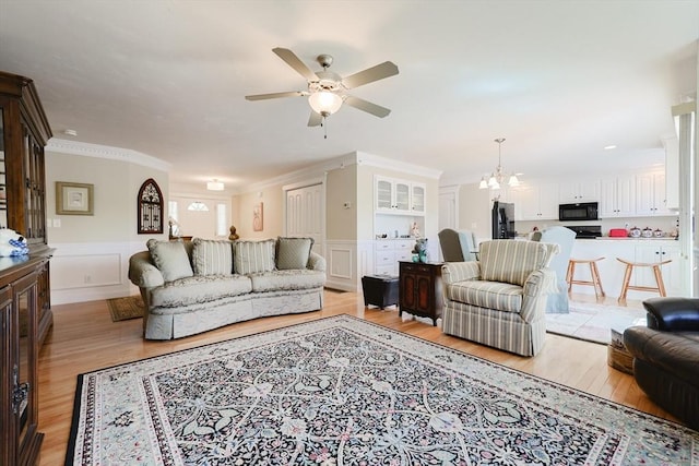 living area featuring light wood finished floors, a ceiling fan, a chandelier, wainscoting, and ornamental molding
