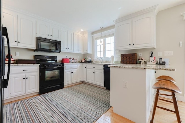 kitchen with black appliances, light wood finished floors, a peninsula, white cabinetry, and a sink