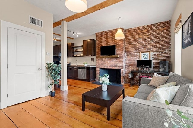 living room featuring light wood-type flooring, visible vents, beam ceiling, and a fireplace