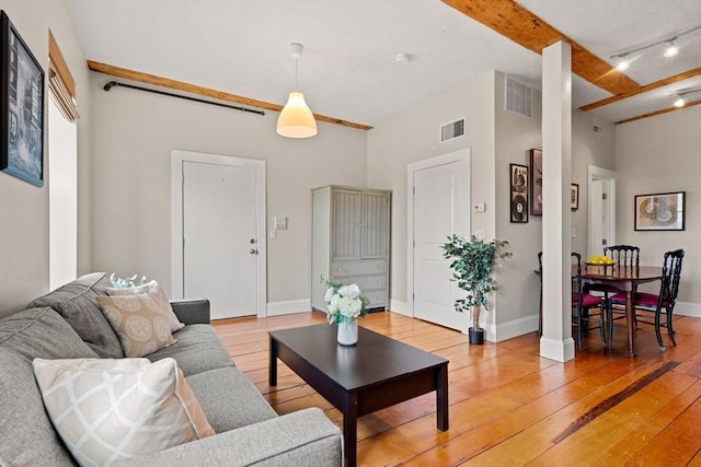 living area featuring visible vents, baseboards, light wood-style floors, and beam ceiling