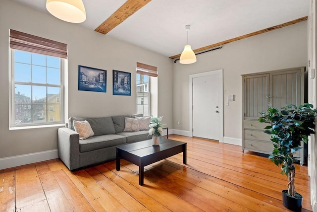 living room featuring beamed ceiling, baseboards, and light wood finished floors