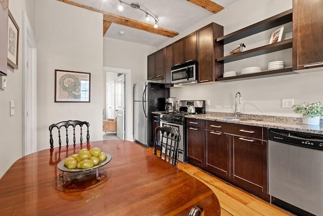 kitchen with a sink, dark brown cabinets, light stone counters, appliances with stainless steel finishes, and open shelves