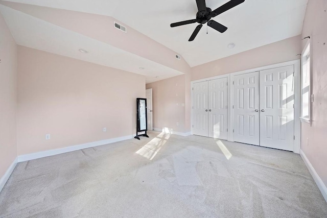 unfurnished bedroom featuring multiple closets, ceiling fan, light colored carpet, and vaulted ceiling