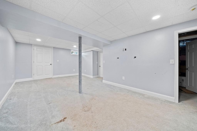 basement featuring a paneled ceiling and light carpet