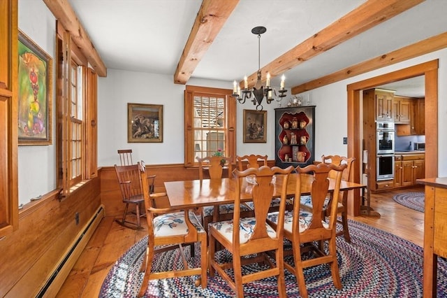 dining space featuring baseboard heating, wainscoting, a chandelier, light wood-style flooring, and beam ceiling