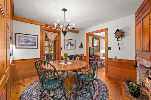 dining space featuring a chandelier, light wood-style floors, a wealth of natural light, and a wainscoted wall