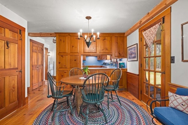 dining room with an inviting chandelier, a wainscoted wall, and light wood-style flooring