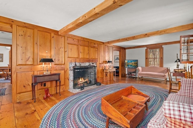 living room with a lit fireplace, light wood-style floors, and beamed ceiling