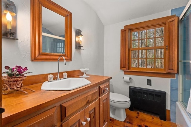 full bathroom with vaulted ceiling, wood finished floors, vanity, radiator, and toilet