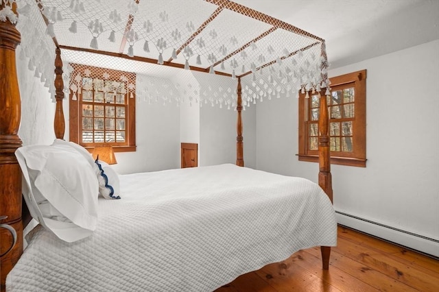 bedroom featuring multiple windows, a baseboard radiator, and wood-type flooring