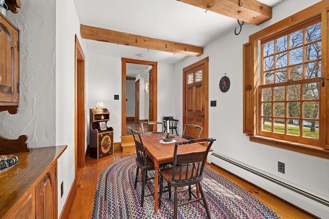 dining room with a baseboard radiator, wood finished floors, beam ceiling, and a wealth of natural light