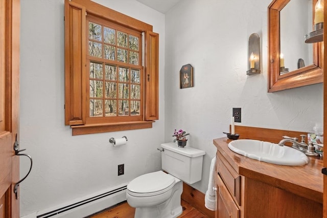 bathroom with a baseboard radiator, toilet, vanity, and wood finished floors