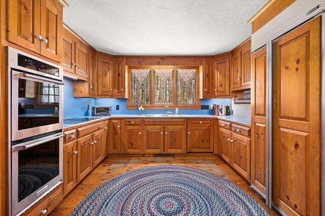 kitchen with double oven, brown cabinets, a sink, and light wood-style floors