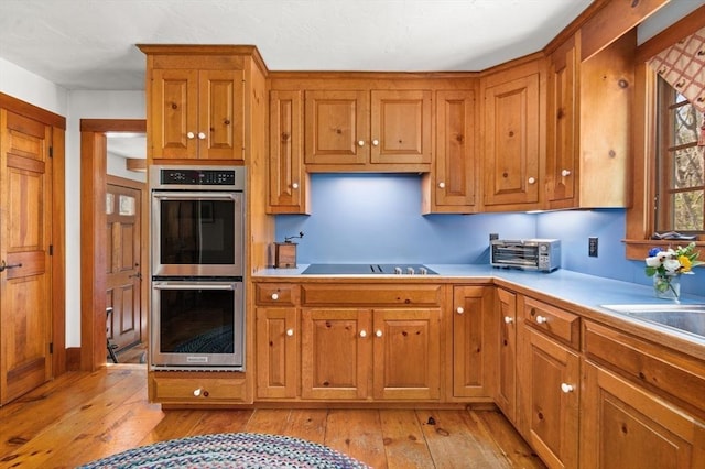 kitchen featuring light wood finished floors, black electric cooktop, brown cabinets, and double oven