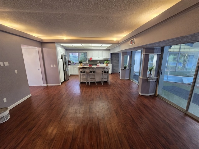 kitchen featuring dark wood-type flooring, white cabinets, a textured ceiling, a kitchen bar, and stainless steel fridge with ice dispenser