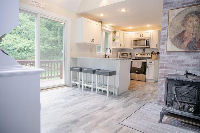 kitchen with stainless steel appliances, white cabinetry, a wood stove, and light stone counters