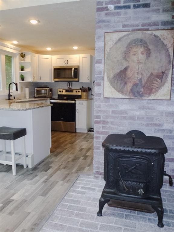 kitchen with sink, white cabinetry, stainless steel appliances, light stone counters, and a wood stove