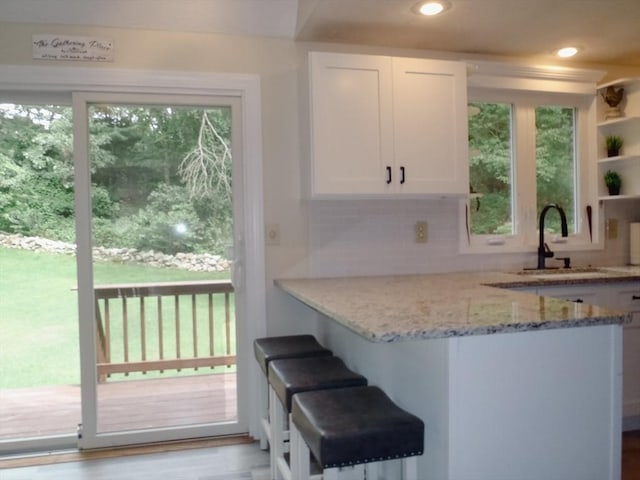 kitchen with sink, white cabinetry, tasteful backsplash, light stone countertops, and light hardwood / wood-style floors