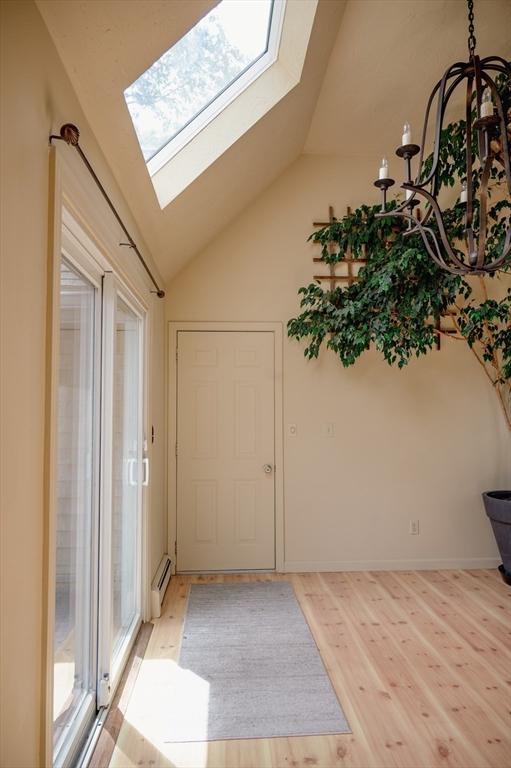 entryway with baseboard heating, lofted ceiling with skylight, and light hardwood / wood-style flooring