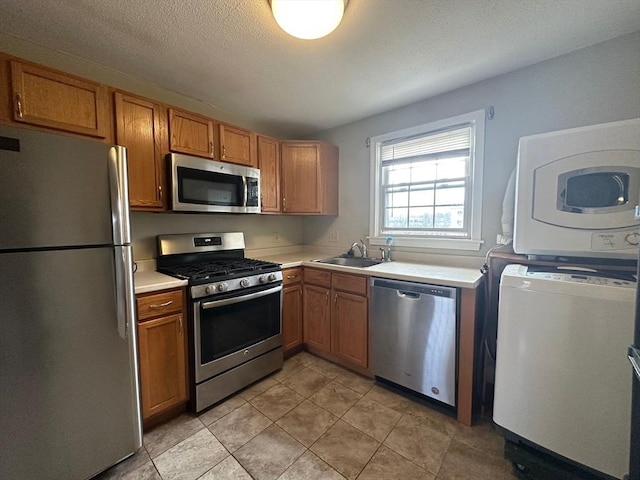 kitchen with appliances with stainless steel finishes, stacked washer / dryer, sink, light tile patterned floors, and a textured ceiling