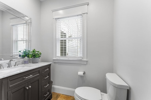 half bath featuring baseboards, toilet, and vanity
