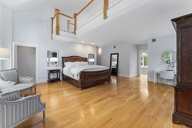 bedroom featuring baseboards, light wood-type flooring, visible vents, and a towering ceiling
