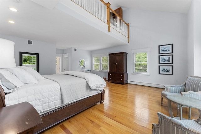 bedroom featuring visible vents, a towering ceiling, recessed lighting, baseboard heating, and light wood-style floors