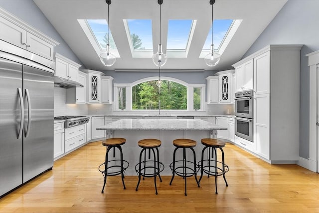 kitchen with light wood finished floors, stainless steel appliances, glass insert cabinets, white cabinetry, and a kitchen breakfast bar
