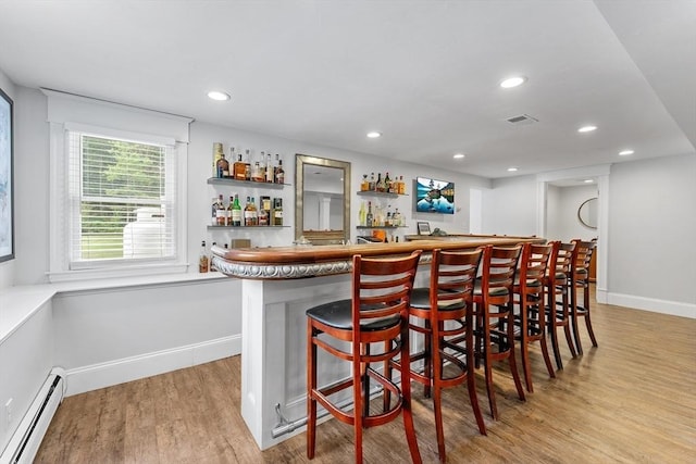 bar featuring wet bar, baseboards, visible vents, light wood-style flooring, and baseboard heating
