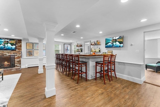dining space with recessed lighting, decorative columns, visible vents, a brick fireplace, and wood finished floors