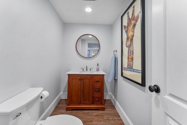 bathroom featuring baseboards, wood finished floors, toilet, and vanity