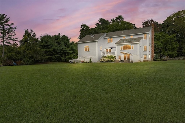 back of property with a chimney and a lawn